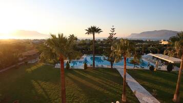 A pool area with palm trees, a tiled pathway, and a view of distant mountains.