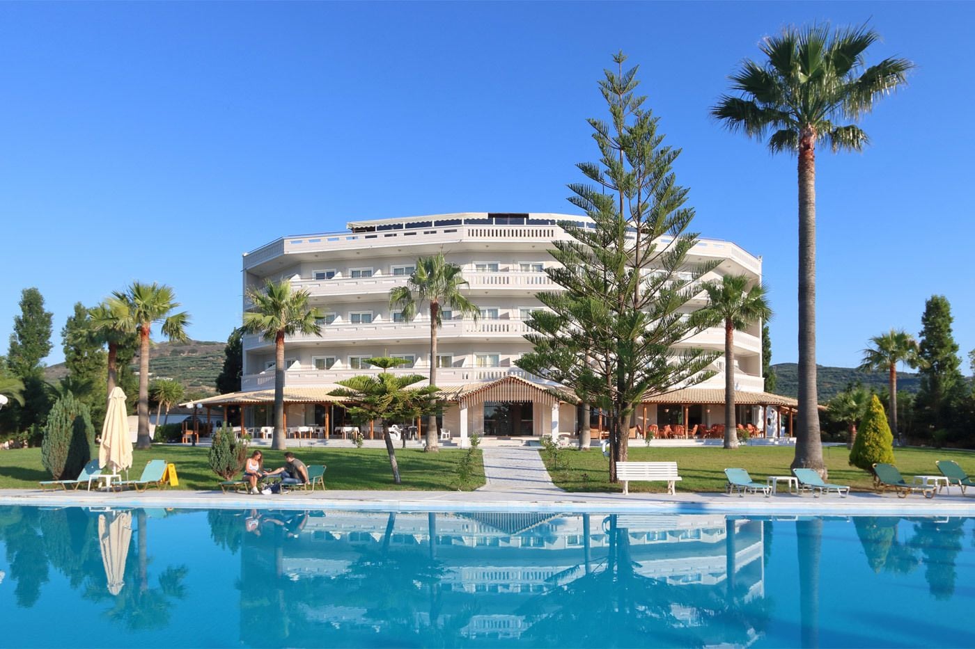 Un hotel con piscina, palmeras y montañas al fondo.