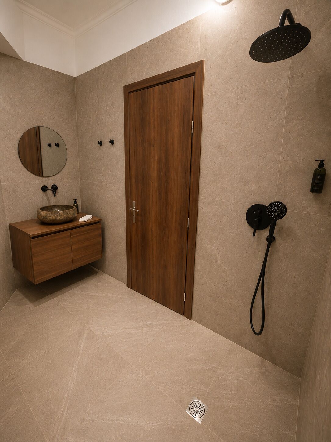 A bathroom with a wooden door, a round mirror, a wooden vanity, a shower head, and a bottle of shampoo.