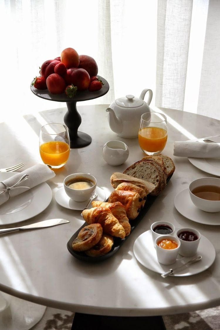 Een ontbijtsetting met een fruitschaal, croissants en koffiekopjes op een tafel.