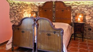 A bedroom with a stone wall, a wooden bed with a headboard, a hanging light fixture, and a small bedside table with a candle. - Villa Denise (Vico Equense)