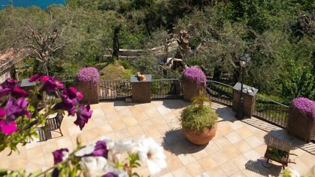 A terrace with potted plants and outdoor furniture overlooking a coastal town and the sea. - Villa Denise (Vico Equense)