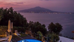 A poolside area with lounge chairs and a view of the sea at dusk. - Villa Denise (Vico Equense)