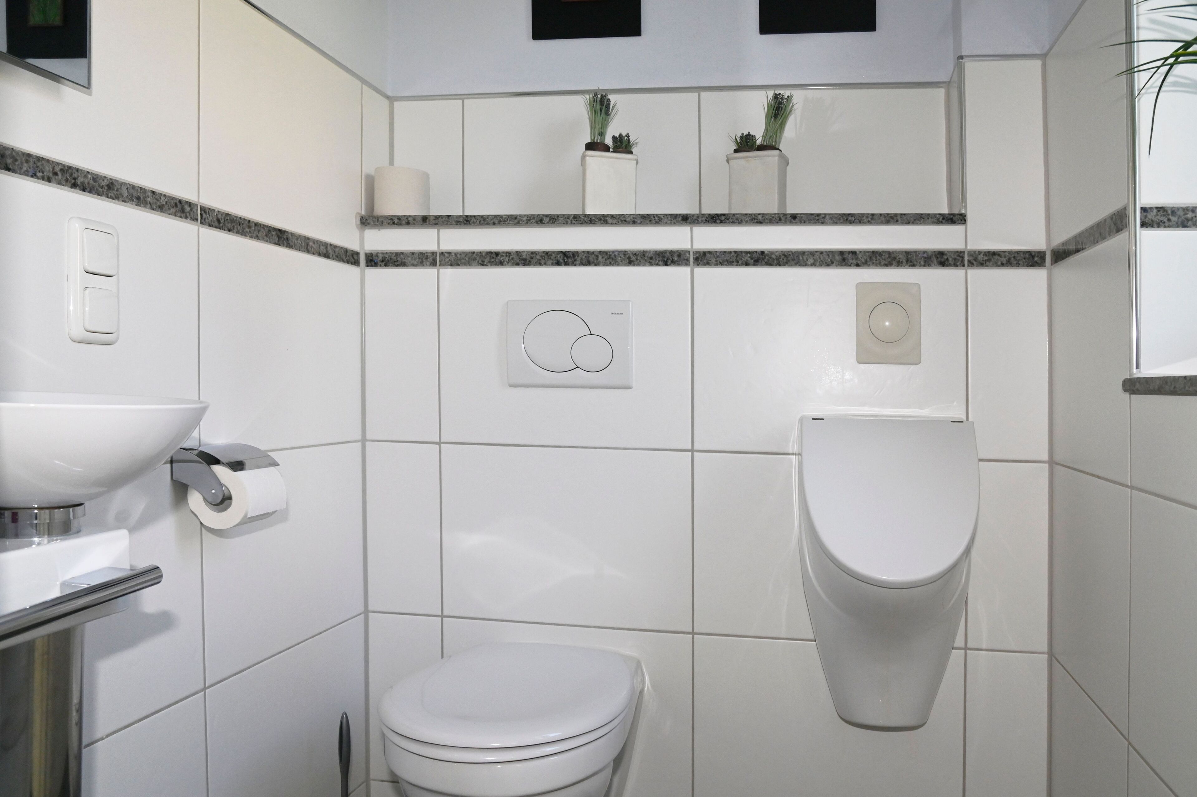 Un baño moderno con azulejos blancos, inodoro, lavamanos y dispensador de papel higiénico.