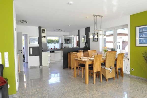 A modern kitchen with white cabinets, a dining area with wooden chairs, and a bright green accent wall. - Dirks holiday home nautical - cottage nautical (Varel)