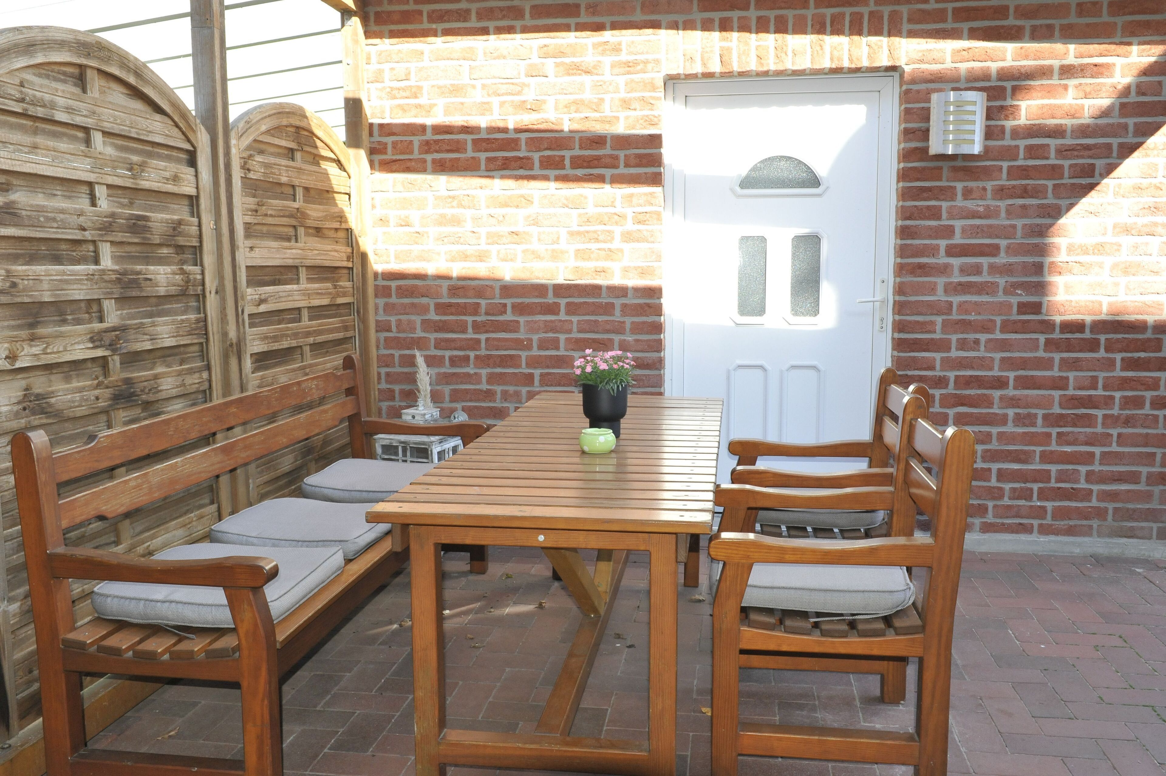 A wooden table with benches, a white door, and a brick wall.
