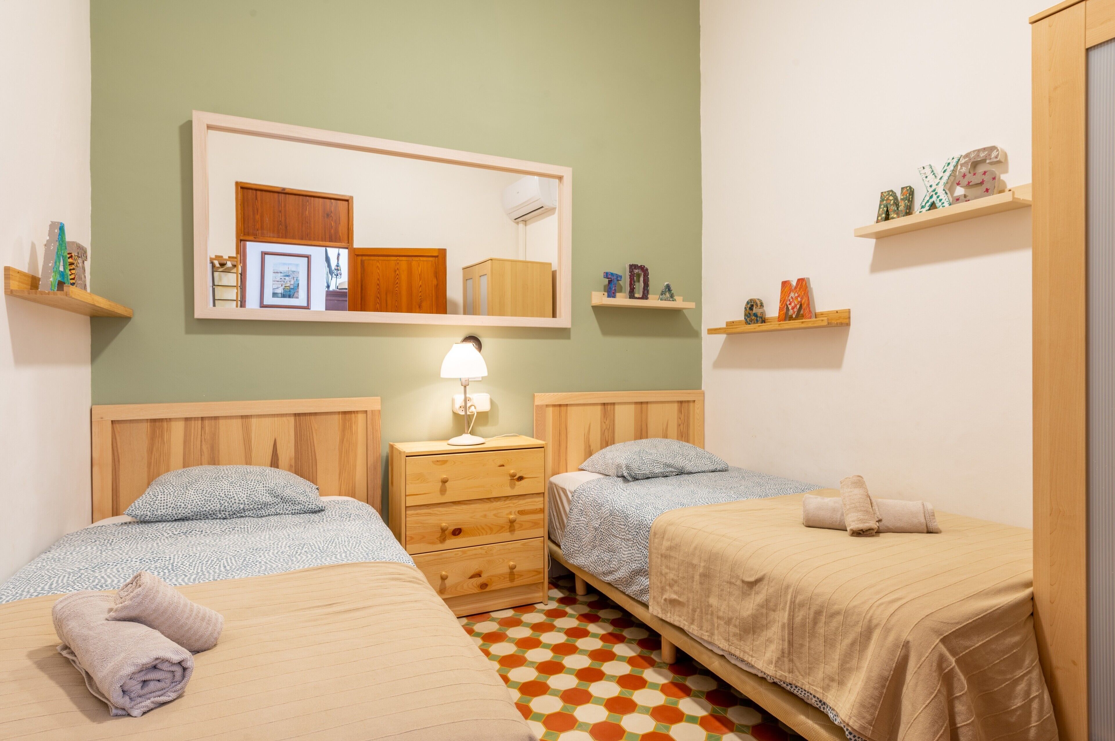 A room with two beds, a wooden dresser, a mirror, and shelves with decorative items.