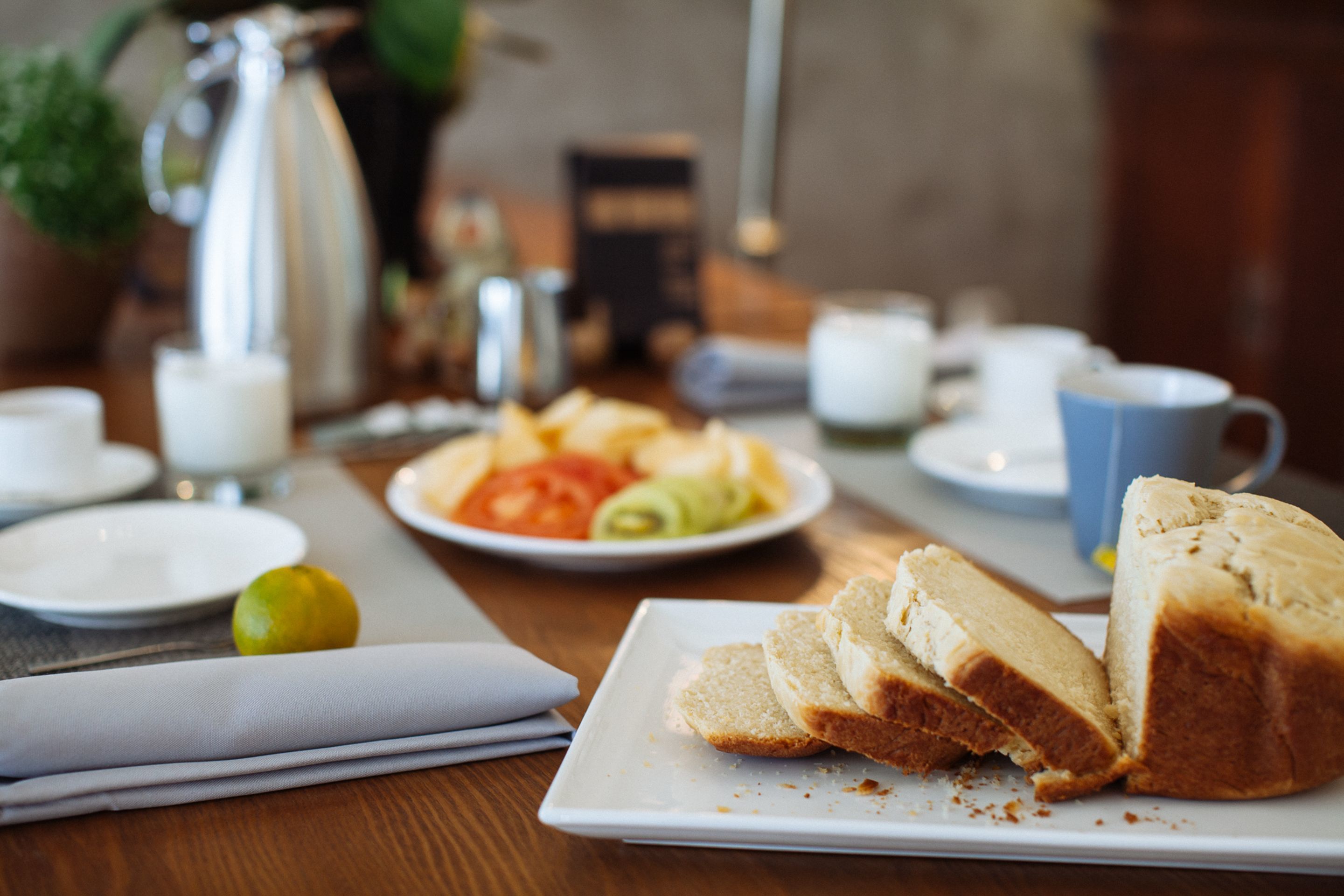A breakfast table with plates of food, a coffee pot, and cups.