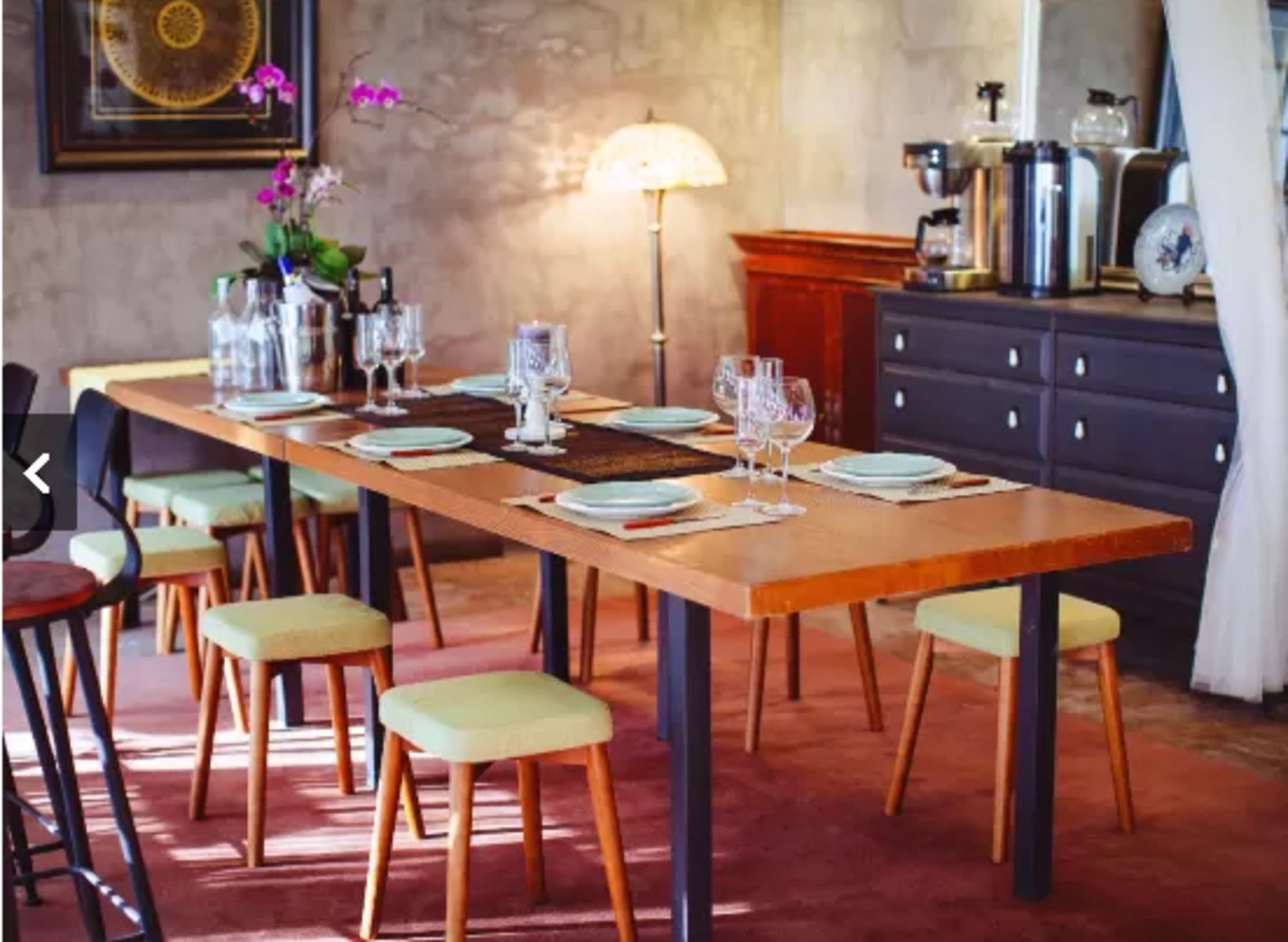 A dining area with a long wooden table set for a meal, surrounded by chairs with cushioned seats.