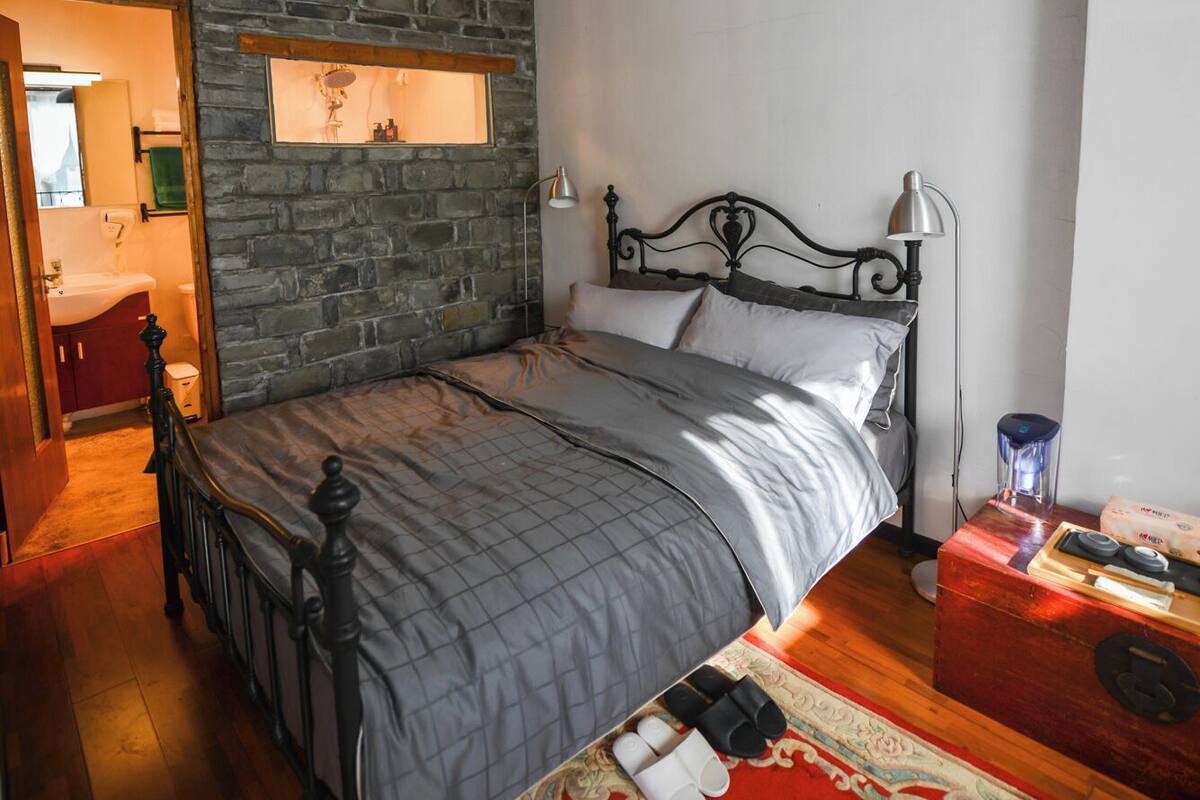A bedroom with a stone wall, a bed with a metal frame, a red carpet, and a wooden floor.