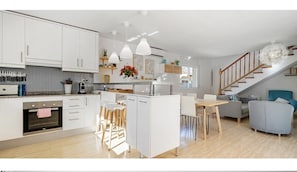 A modern kitchen with white cabinets, a central island, pendant lights, and a staircase leading to a living area with a sofa and a coffee table.