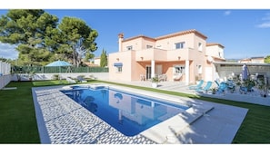 A two-story house with a swimming pool, outdoor seating, and a well-maintained lawn.