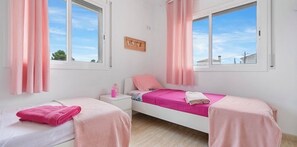 A bedroom with two beds, pink bedding, a nightstand, and a window with curtains.