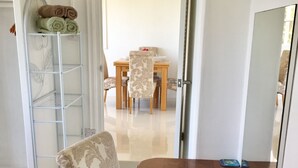 A dining area with a wooden table and patterned chairs, a metal shelf with towels, and a view into a dining room with a table and chairs. - Apartment with a million dollar view and a wrap-around balcony with beach access (Castries)