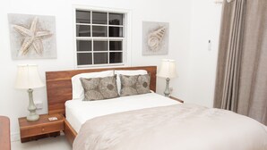 A neatly made bed with a wooden headboard, two bedside lamps, and a window with a view of the outside. - Apartment with a million dollar view and a wrap-around balcony with beach access (Castries)