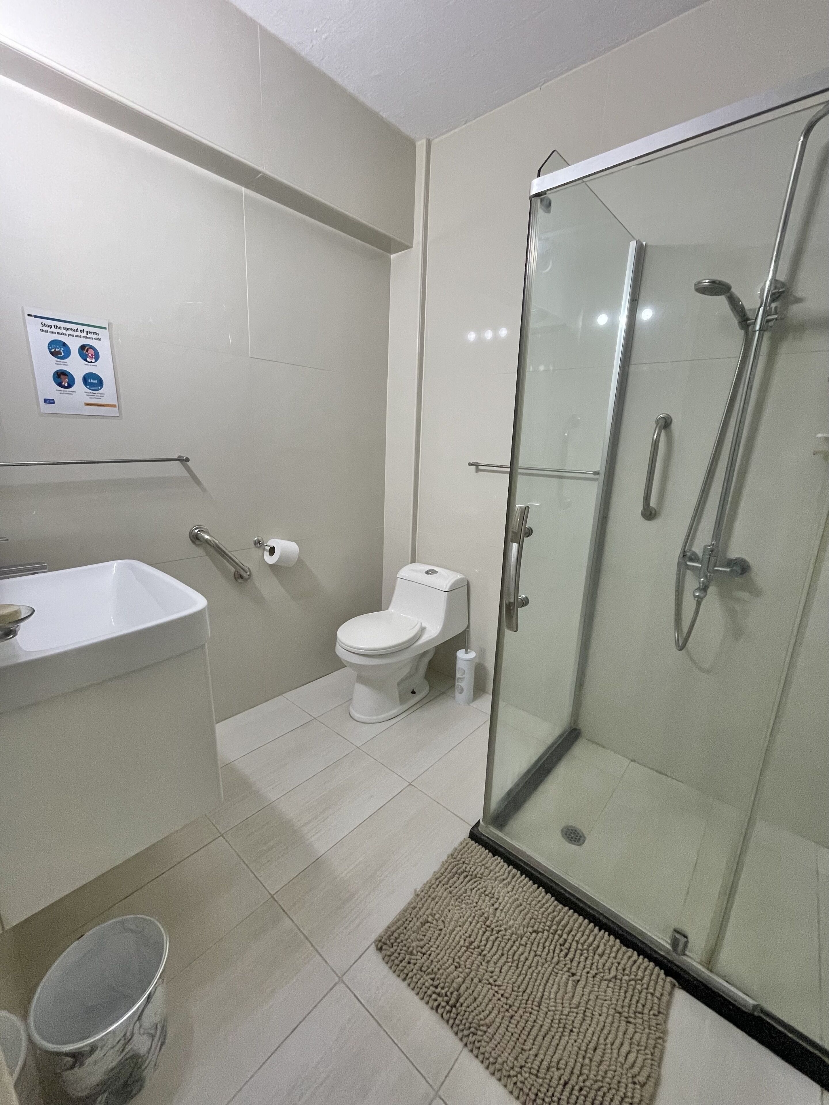 A modern bathroom with a glass shower enclosure, a toilet, a sink, and a hand dryer.