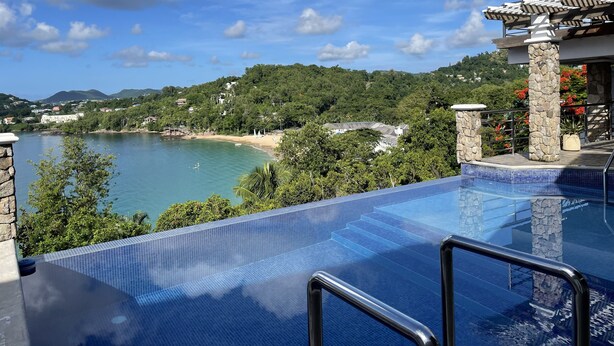 A clear view of a swimming pool with a stone balustrade and a view of a beach and mountains in the background. - Apartment with a million dollar view and a wrap-around balcony with beach access (Castries)