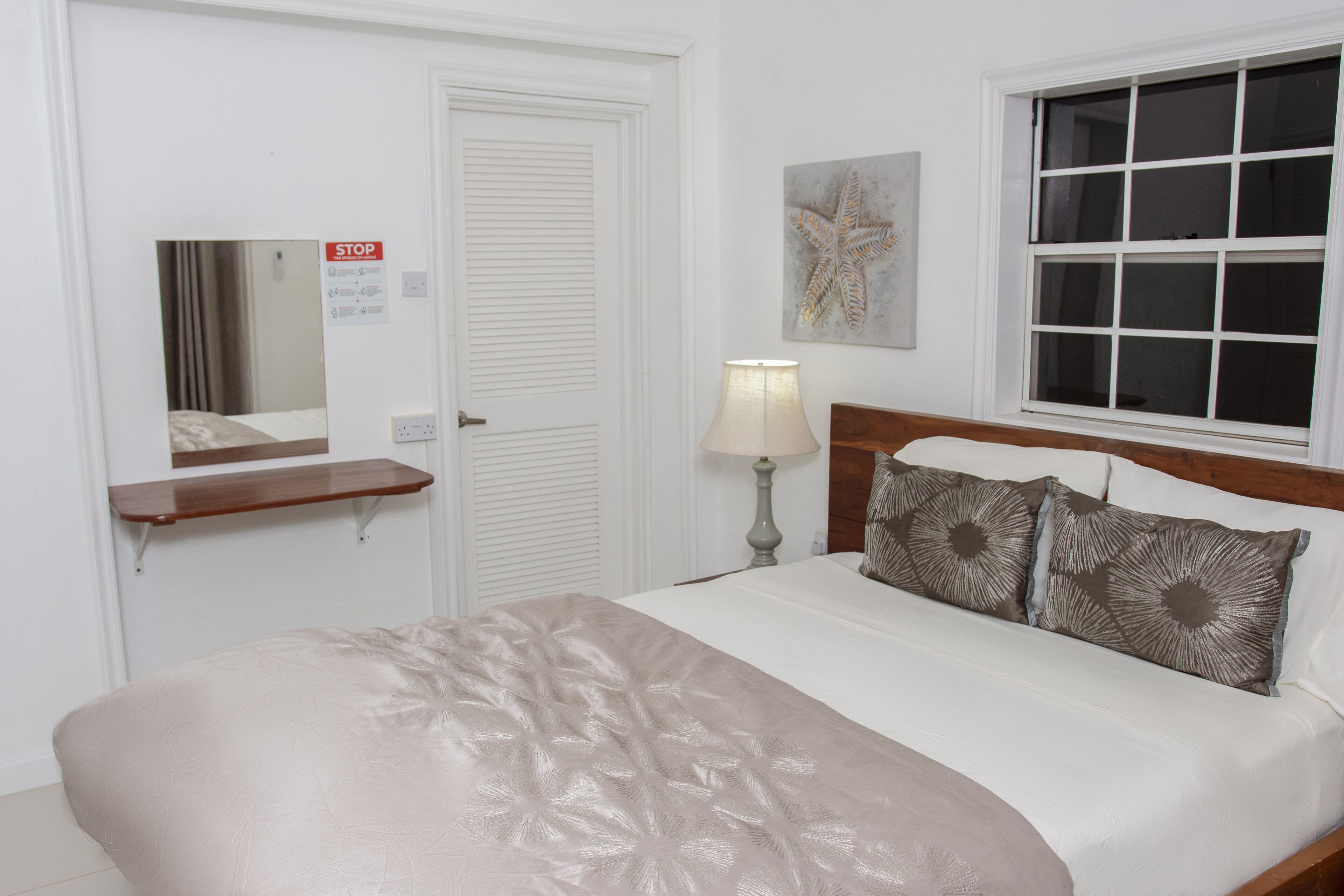 Una habitación de hotel con una cama, una mesita de noche, una lámpara, una ventana y una puerta.