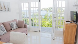 A modern living room with a pink sofa, a wooden cabinet, and a view of the sea through large glass doors. - Apartment with a million dollar view and a wrap-around balcony with beach access (Castries)