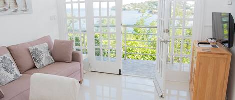 Un salón moderno con un sofá rosa, un mueble de madera y vista al mar a través de amplios ventanales.