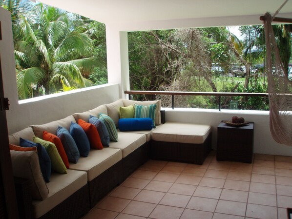 A sunlit room with a beige sofa, colorful cushions, a small table with fruit, and a view of lush greenery outside. - Beautiful Villa in the Wyndham Rio Mar Resort (Rio Grande)