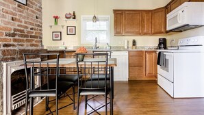 A kitchen with a brick wall, wooden cabinets, a white stove, and a dining area with chairs and a table.