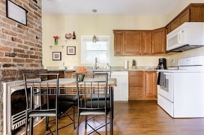 A kitchen with a brick wall, wooden cabinets, a white stove, and a dining area with chairs and a table.