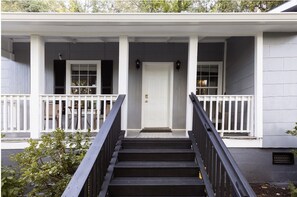 A two-story house with a front porch, a staircase leading to the entrance, and a door with a small porch area.