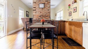 A dining area with a brick wall, wooden flooring, and a kitchen with wooden cabinets and a granite countertop.