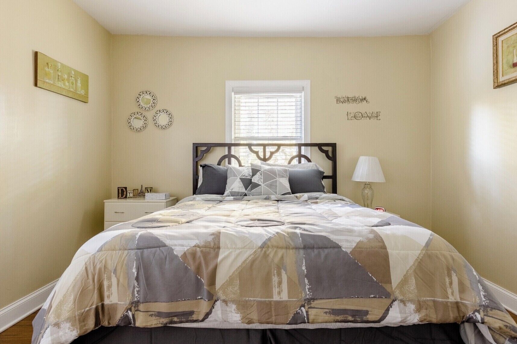 Une chambre à coucher comprenant un lit, une table de chevet, une lampe et des œuvres d’art décoratives accrochées au mur.
