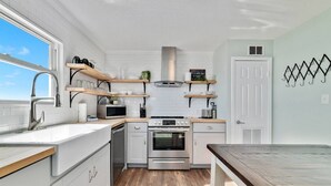 A compact kitchen with white cabinets, a stainless steel sink, a microwave, and a stove. There are wooden shelves above the counter and a chalkboard on the wall. - Sunrise Village 201 - Private balcony right on the (Gulf Shores)
