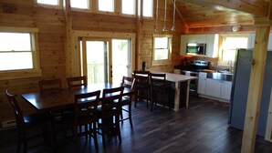 L’intérieur d’une cabane en bois comprend une table à manger, des chaises, un coin cuisine et de grandes fenêtres.