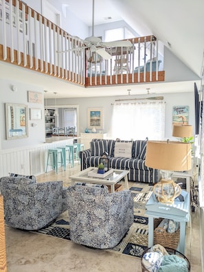 A spacious living area with striped sofas, a coffee table, and a high ceiling with a fan.
