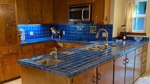 Una cocina con armarios de madera, un lavamanos de acero inoxidable y un salpicadero de azulejos azules.