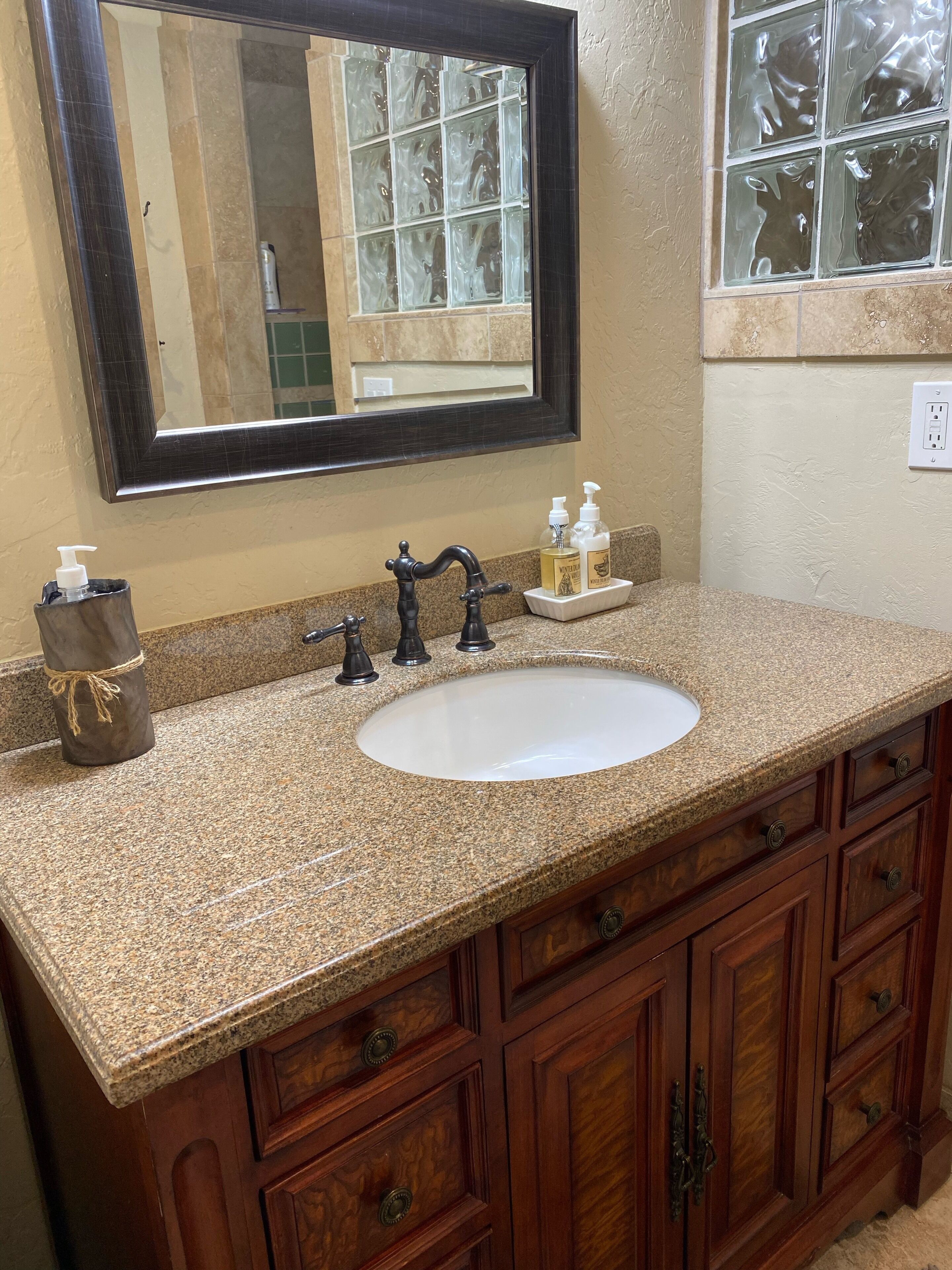 A bathroom with a granite countertop, a white sink, a dark wooden vanity with multiple drawers, a mirror, and a window with frosted glass.