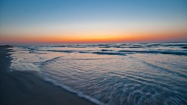 Une plage avec des vagues au coucher du soleil.