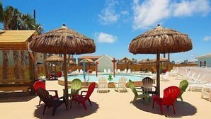 Un espace aménagé au bord de la piscine, avec des parasols en chaume, des chaises longues et un ciel d’un bleu limpide.