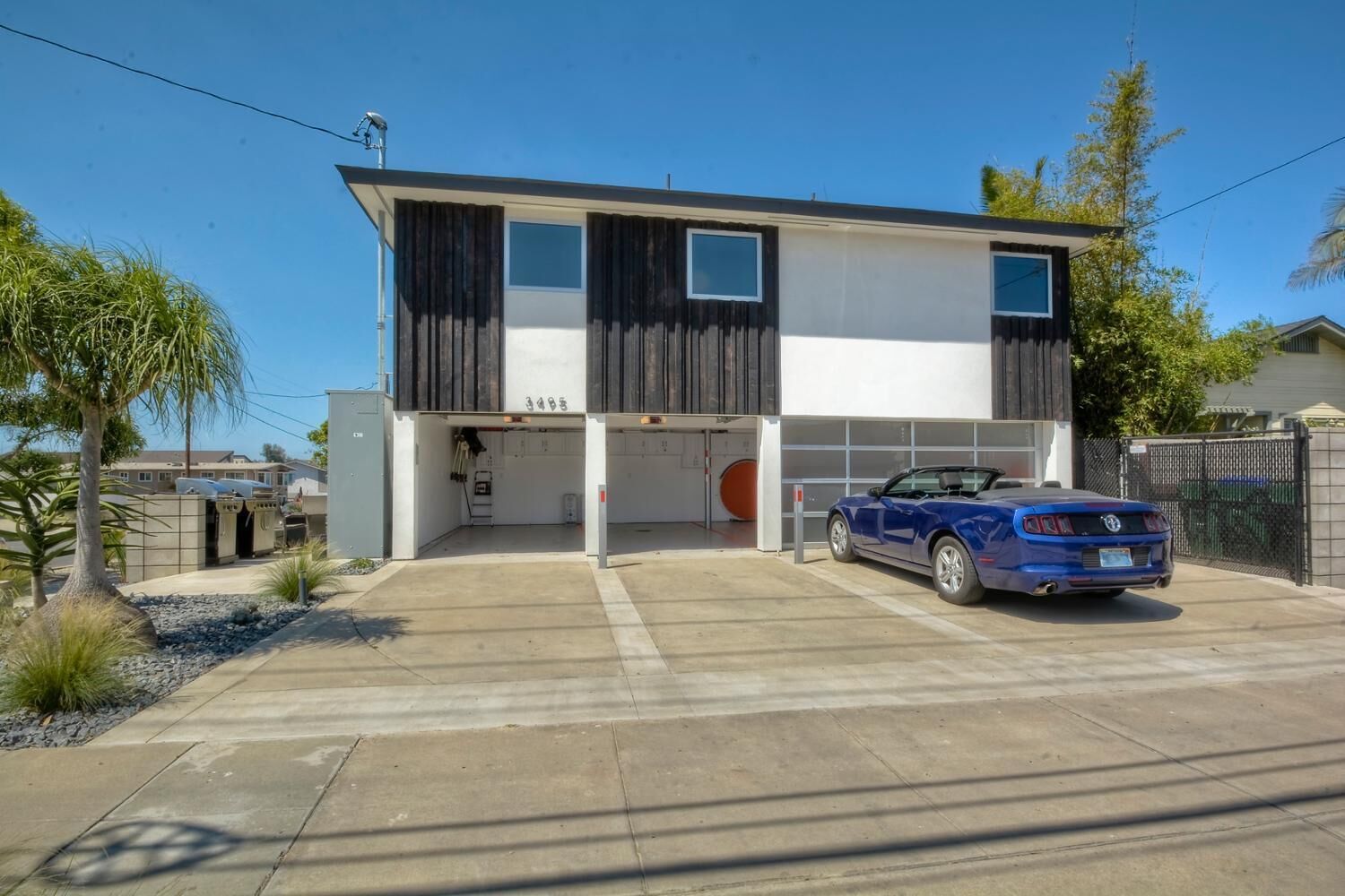 Une maison moderne à deux étages avec un garage, une voiture bleue garée devant, et un ciel dégagé.
