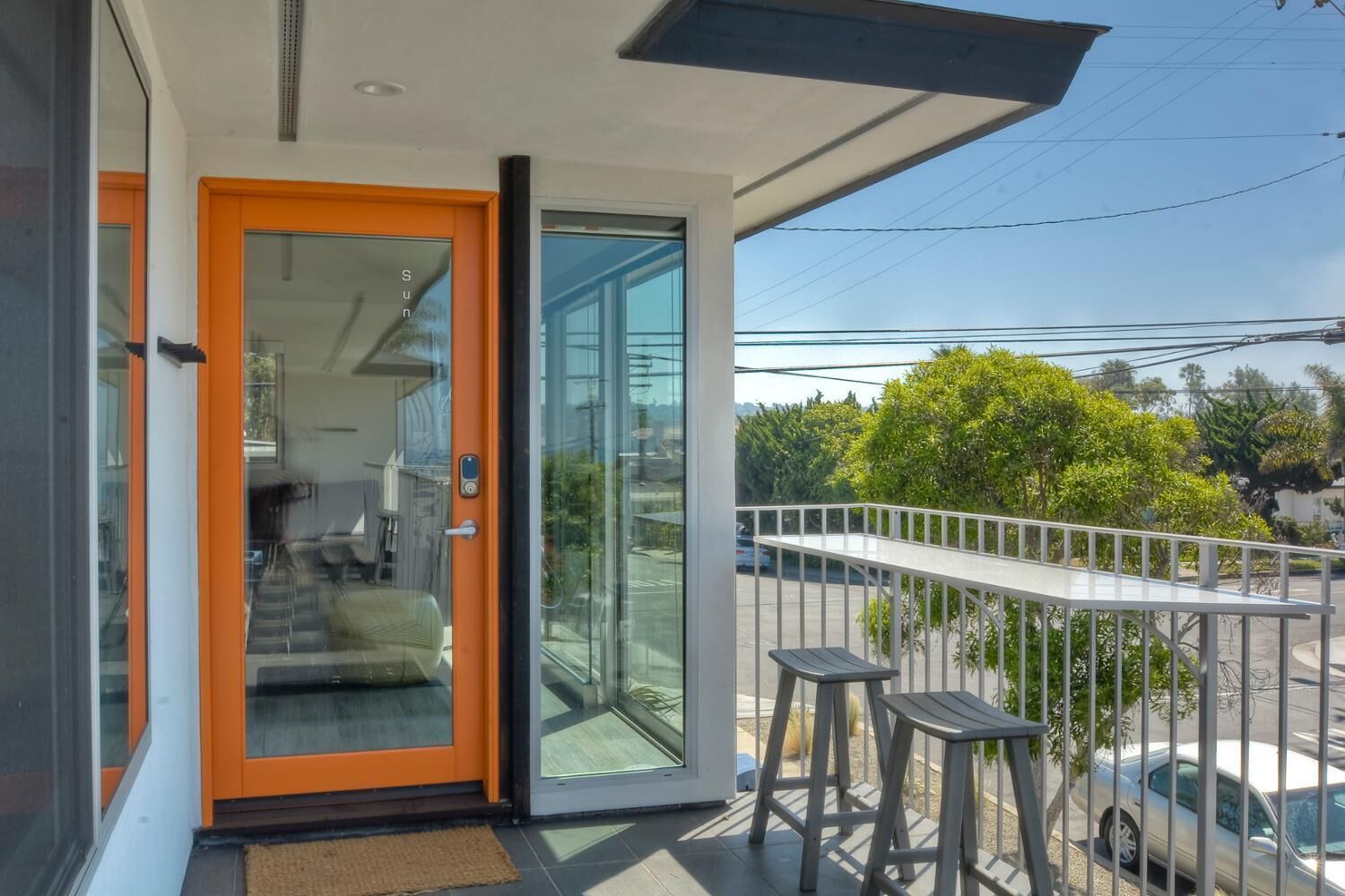 A modern apartment with a glass door leading to a living area, a balcony with a railing, and a view of the street.