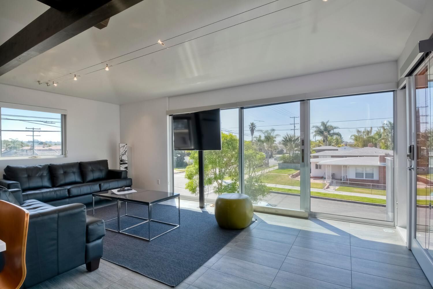 Una sala moderna con un sofá de cuero negro, una mesa de centro de vidrio y un ventanal con vistas a una zona residencial.