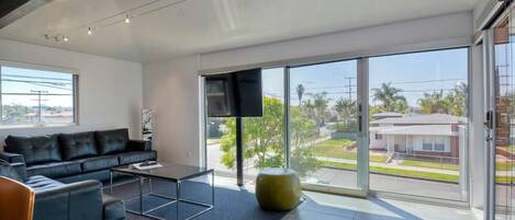Una sala moderna con un sofá de cuero negro, una mesa de centro de vidrio y un ventanal con vistas a una zona residencial.