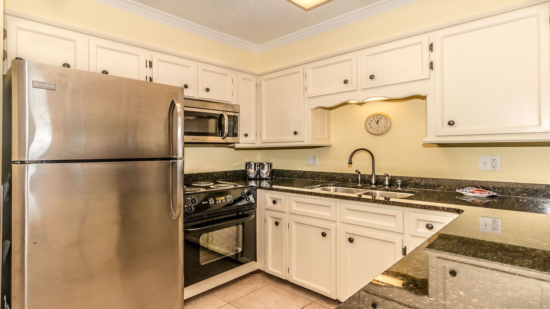 A kitchen with white cabinets, a stainless steel refrigerator, a microwave, a stove, and a sink.