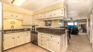 A kitchen with white cabinets, a granite countertop, and a dishwasher. There is a clock on the wall and a painting above the counter. - Beachfront/Pool Murrells/GardenCity/Surfside 
Wkly/MilitaryFirePoliceNurse Discs (Murrells Inlet)