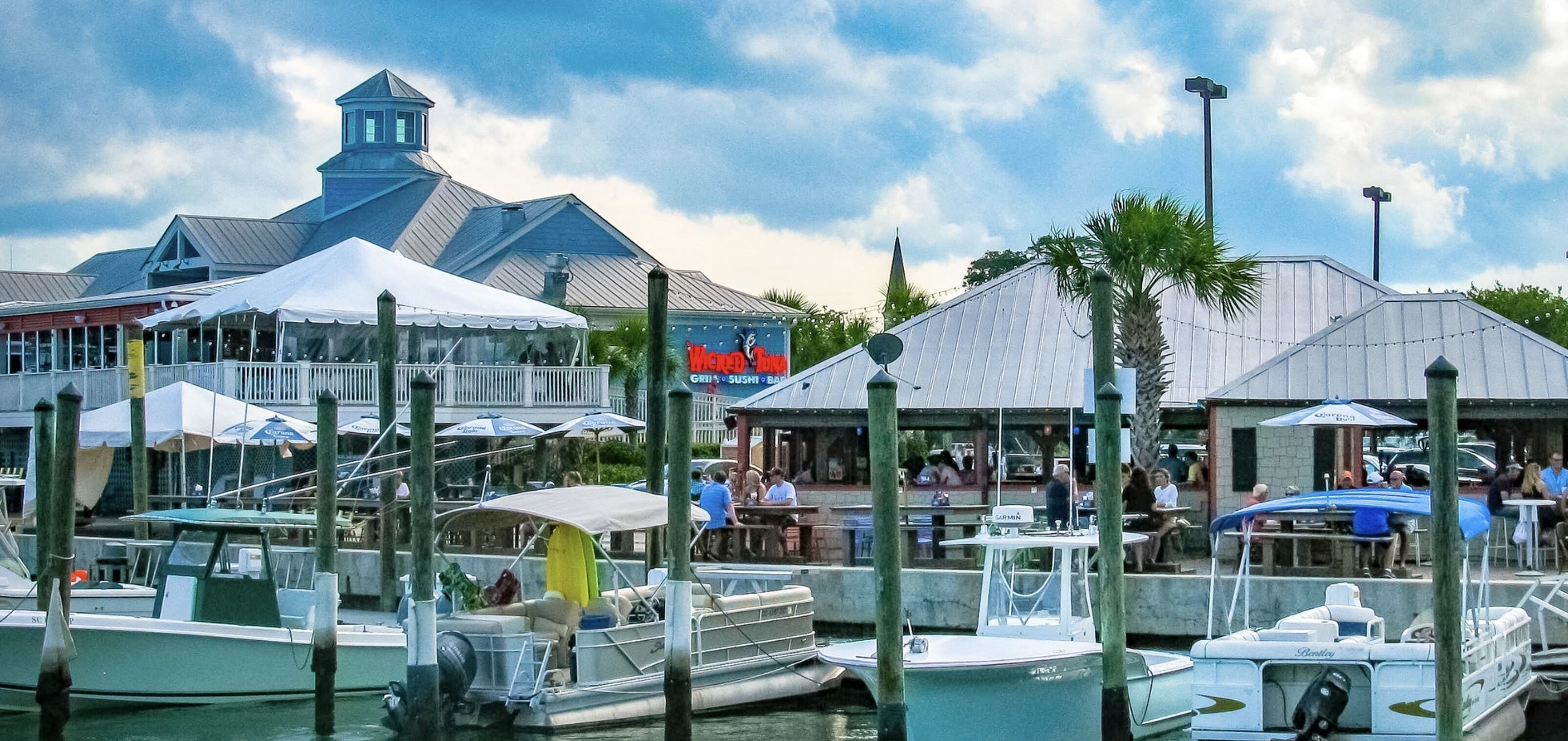 A marina with boats docked, a restaurant with outdoor seating, and a building with a pointed roof.