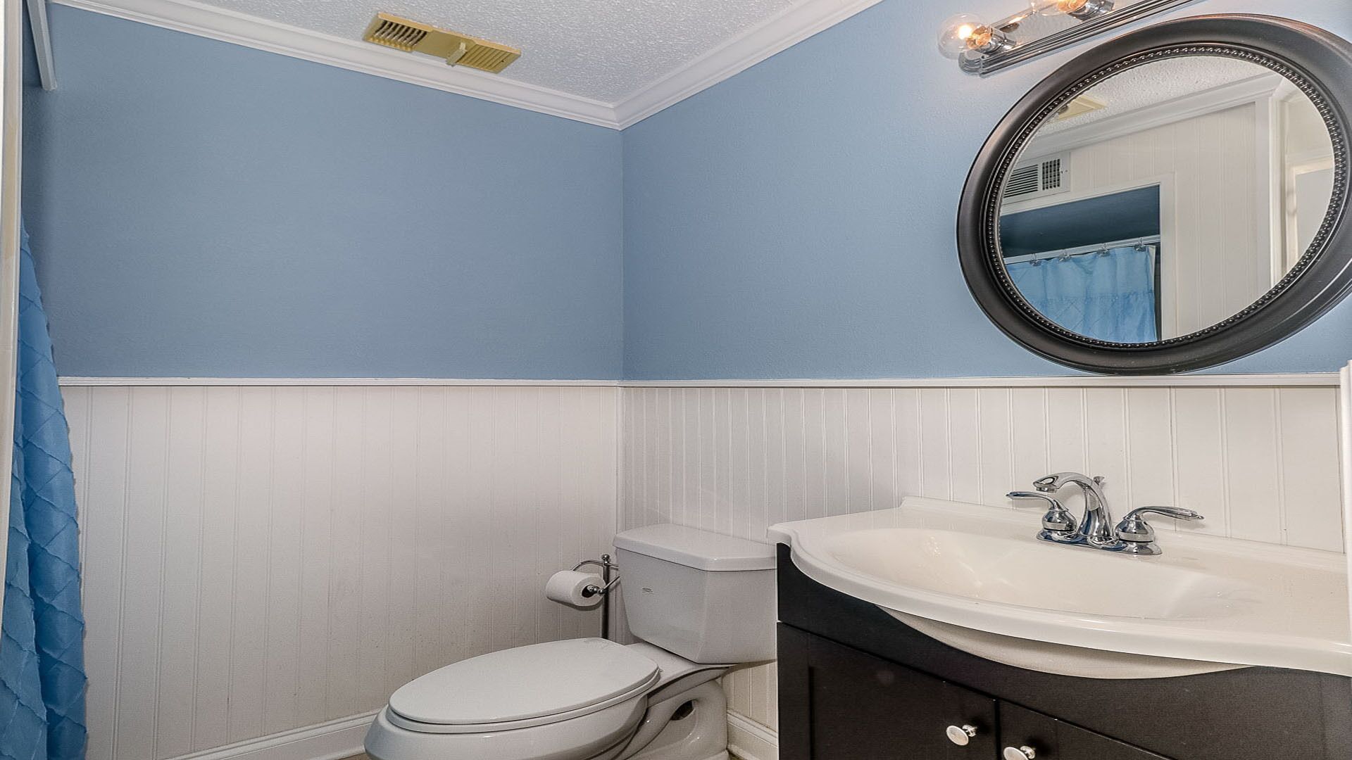 A bathroom with a white toilet, a white sink, and a mirror with lights.