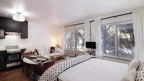 Ein Schlafzimmer mit Bett, Schreibtisch, Stuhl, Fernseher und einem Fenster mit Vorhängen.