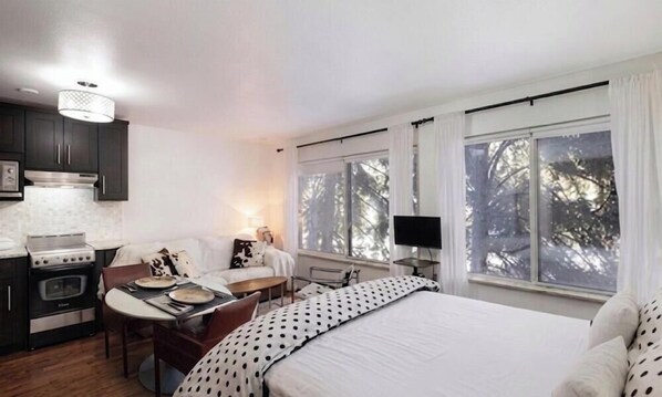 Ein Schlafzimmer mit Bett, Schreibtisch, Stuhl, Fernseher und einem Fenster mit Vorhängen.