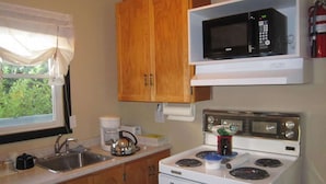 A kitchen with wooden cabinets, a microwave, a stove, and a window with curtains.