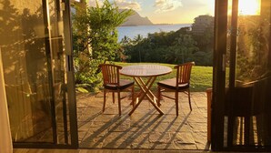 Un patio al aire libre con una mesa y sillas, con vistas panorámicas al océano y a la montaña.