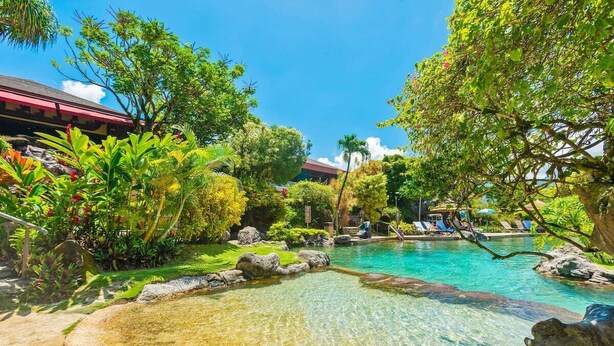Una piscina cristalina rodeada de vegetación tropical y un edificio con techo rojo.